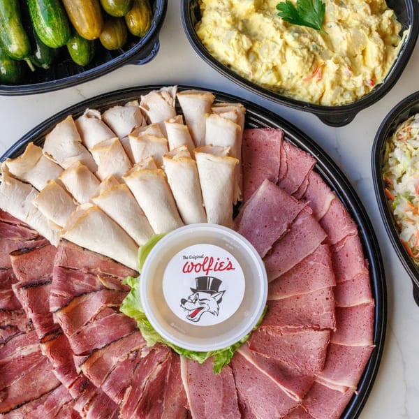A deli platter with sliced meats, potato salad, coleslaw, and pickles from The Original Wolfie's.