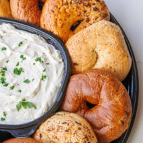 A black platter with assorted bagels and a bowl of cream cheese topped with chives.
