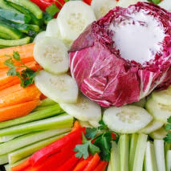 A vibrant vegetable platter with sliced cucumbers, carrots, celery, red peppers, and a radicchio dip.