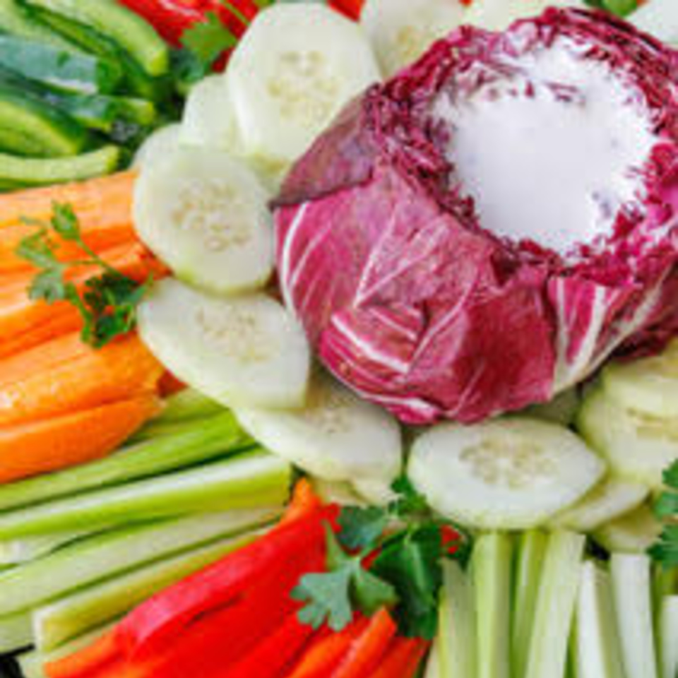 A vibrant vegetable platter with sliced cucumbers, carrots, celery, red peppers, and a radicchio dip.