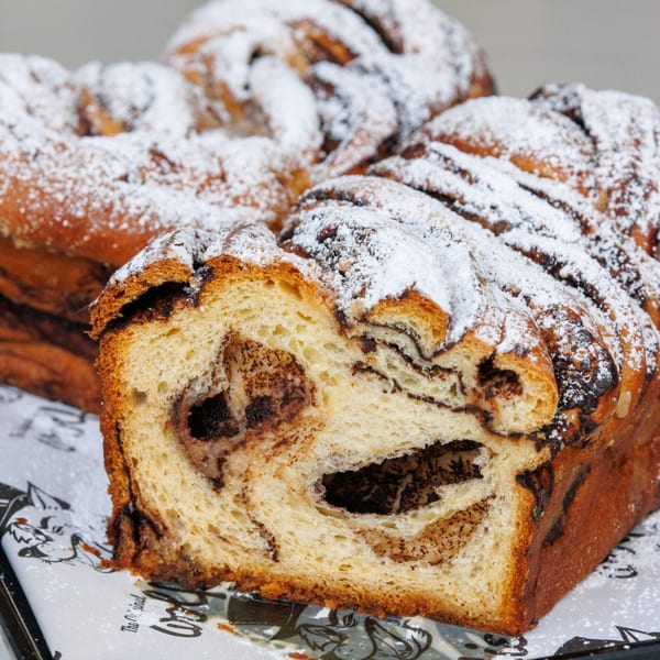 Close-up of a sliced chocolate babka loaf, dusted with powdered sugar, from Wolfie's deli.