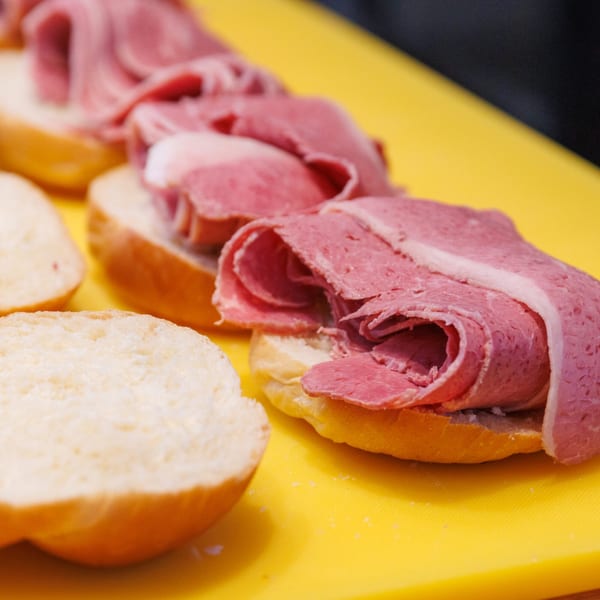 Several deli sandwiches with thinly sliced corned beef on buns, ready for assembly on a yellow cutting board.