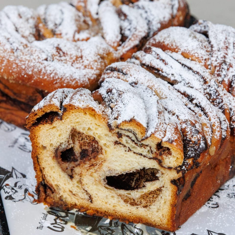 A sliced chocolate babka loaf from The Original Wolfie's, dusted with powdered sugar.