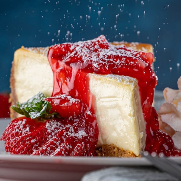 A slice of cheesecake with strawberry topping, powdered sugar, and mint, from The Original Wolfie's.
